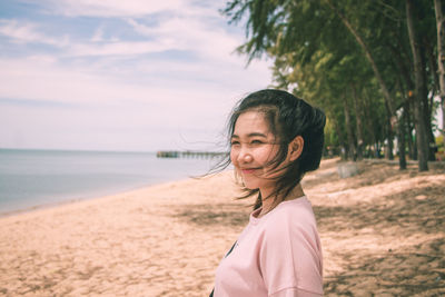 Young woman standing on beach against sky