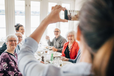 Owner clicking photograph of senior friends sitting in restaurant