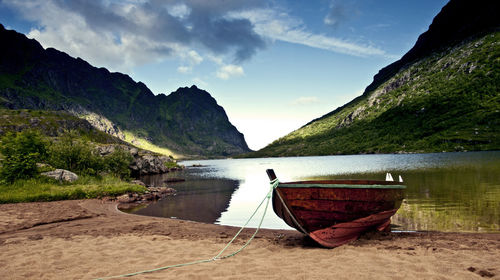 Boat moored on lake by mountains against sky