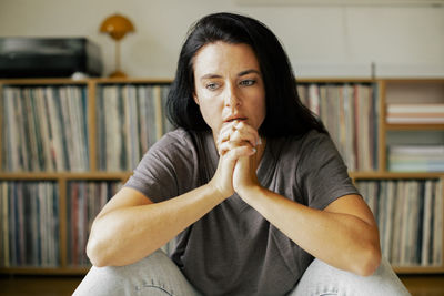 Worried woman with hands clasped sitting at home