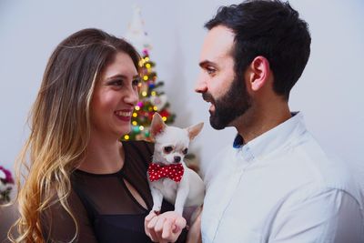 Smiling couple with chihuahua standing against wall at home