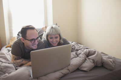 Young couple lying in bed looking at a laptop