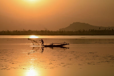 A boatman throws fishing net into water during sunset at dal lake in srinagar.