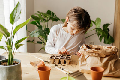 Girl planting seeds for seedlings in small recyclable peat pots, seedling container.