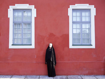 Woman wearing burka standing against red building