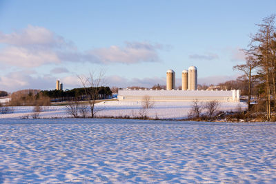 Snow covered field by building against sky