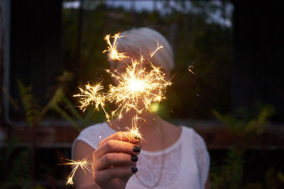 Close-up of woman holding sparkler at night
