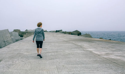 Woman walking on retaining at beach wall against sky