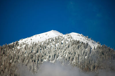 Low angle view of snowcapped mountains against clear blue sky