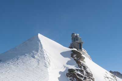 Low angle view of building on snowcapped mountain against clear blue sky