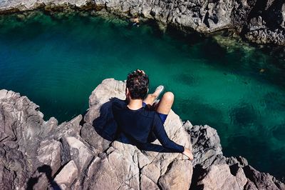 Rear view of man sitting on rock