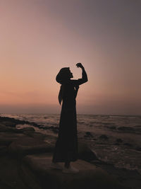 Silhouette woman standing on beach against sky during sunset