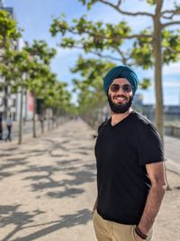 Portrait of young man sikh man wearing a turban and a full smile standing against sky and trees. 