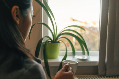 Asian woman is drinking hot coffee and looking out to the window in a cozy morning.