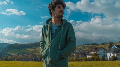 Young man standing by house on field against sky