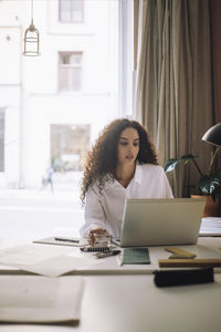 Female design professional working on laptop while sitting at desk in office