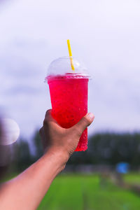 Cropped hand of person holding cold drink against sky