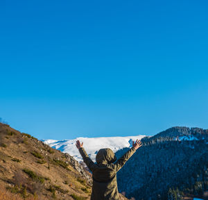 Rear view of man standing on mountain against blue sky