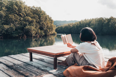 Rear view of man sitting by lake against sky