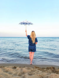 Rear view of woman with umbrella standing at beach against sky