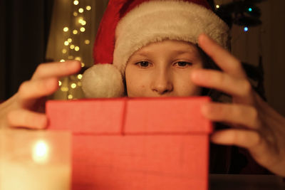 Little girl in santa hat opening red christmas gift box and looking inside in surprise. merry