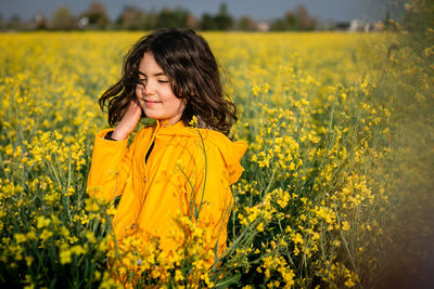 Girl in raincoat standing amidst yellow flowering plants on field