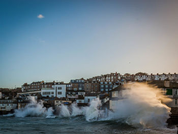 Waves splashing on shore by residential district against sky