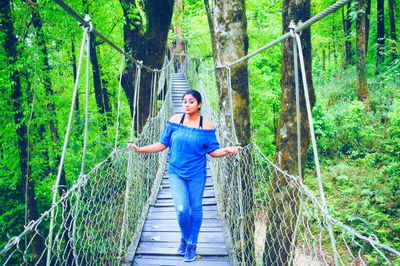 Young woman standing on footbridge in forest