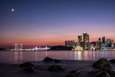 Illuminated city by river against sky at night