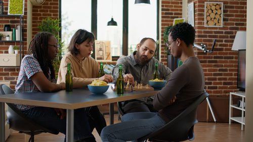 Side view of friends using mobile phone while sitting on table