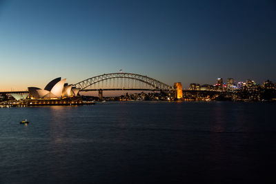 Illuminated bridge over cityscape against clear sky at night
