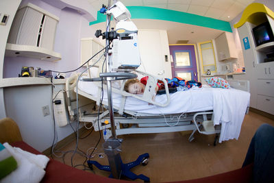 Toddler sleeps alone in full-sized hospital bed hooked up to ivs.