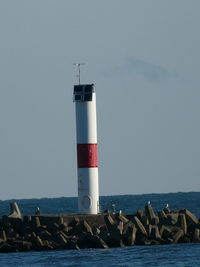 White and red lighthouse on rocky breakwater with gulls under blue sky