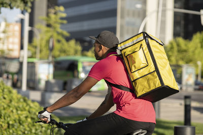 Delivery man with yellow backpack riding bicycle during sunny day