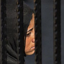 Close-up of sad woman in hijab seen through fence