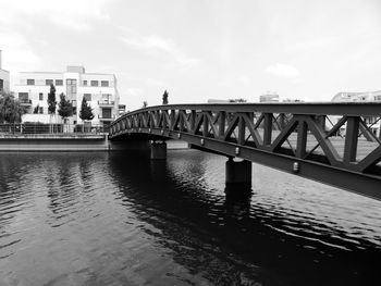 Bridge over river by buildings against sky