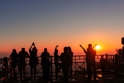 Silhouette people standing by railing against sky during sunset