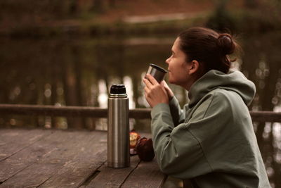 Young woman smiling drinking tea from thermos with muffin outdoors