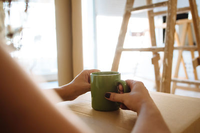 Cropped image of woman with coffee cup on table at home