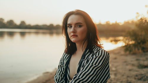 Portrait of young woman standing against lake