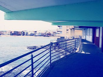 Railing by sea against blue sky in city