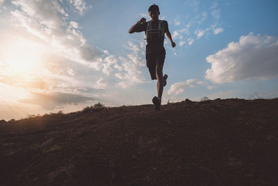 Low angle view of man jumping on land against sky during sunset