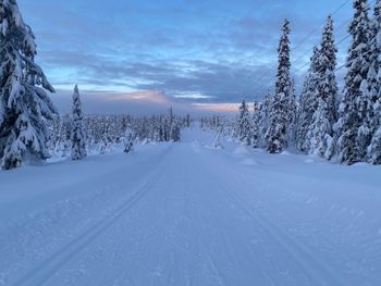 Snow covered landscape against sky during sunset