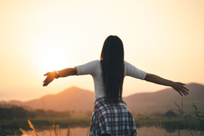 Rear view of woman with arms outstretched against sky during sunset