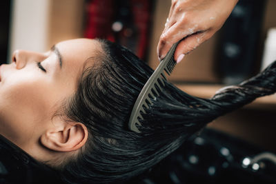 Cropped hand of hairdresser combing woman hair in salon