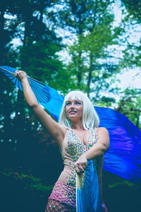 Woman with blue hand fan posing in forest