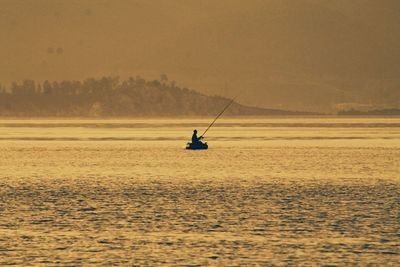 Silhouette man on sailboat in sea against sky during sunset