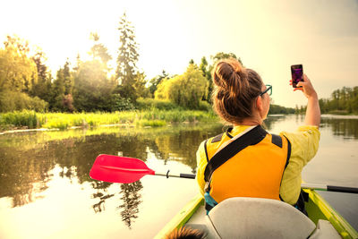 Rear view of woman taking selfie in lake