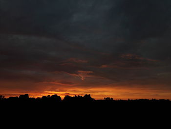 Silhouette landscape against dramatic sky during sunset