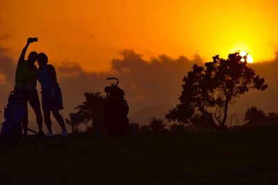 Silhouette people by tree against sky during sunset